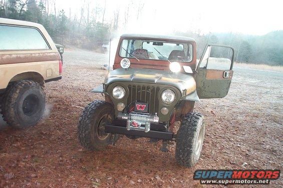 Jeep CJ-5 with winch and open door, parked next to a Ford Bronco