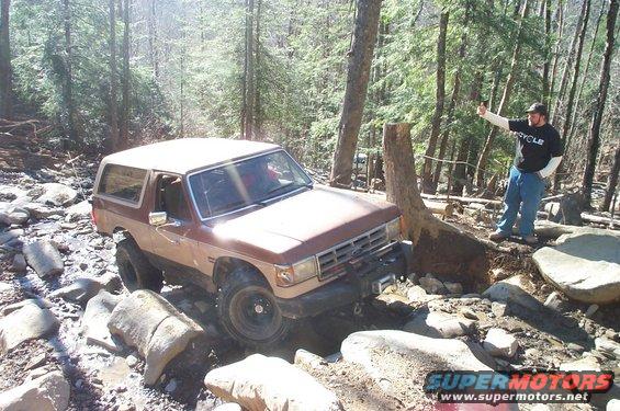 1987 Ford Bronco navigating a rocky trail with a man standing nearby
