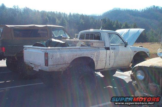 White pickup truck parked next to a dark SUV and a green vehicle. Hood is open on the truck