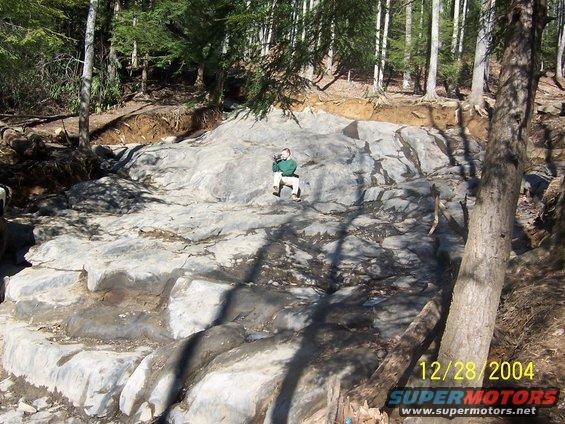 Person sitting on a large rock formation in a wooded area