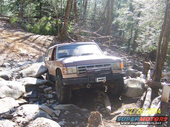 1987 Ford Bronco navigating rocky stream bed, front winch visible