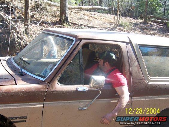 Man in red shirt looking through binoculars from driver's seat of a brown 1987 Ford Bronco