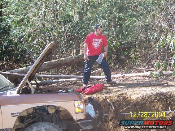 Brown 1987 Ford Bronco with hood open, parked on a dirt embankment with a man standing nearby
