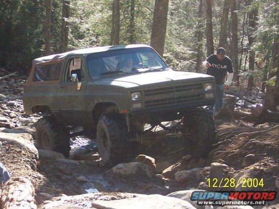 Olive green SUV with large tires navigating a rocky trail in a forest