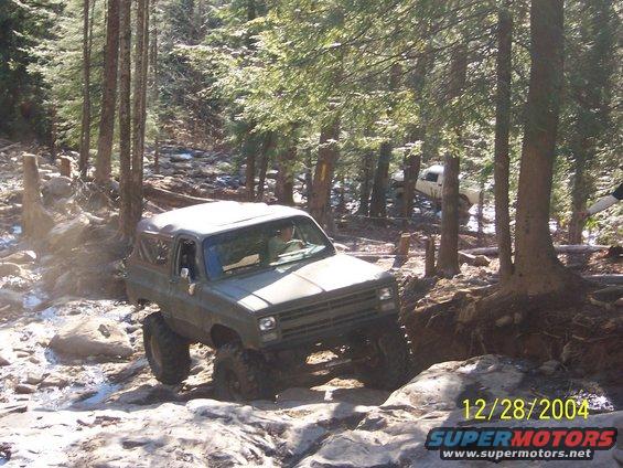 Olive green off-road SUV with large tires navigating a rocky trail, driver visible
