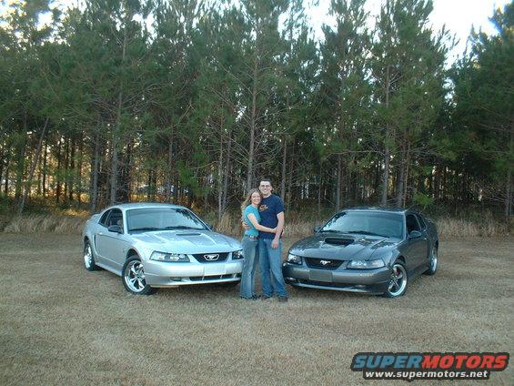 Couple standing between a silver and a gray 1999 Ford Mustang