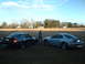 1999 Ford Mustang - Two 1999 Ford Mustangs are parked on a grassy field with a woman standing between them under a partly cloudy sky.
