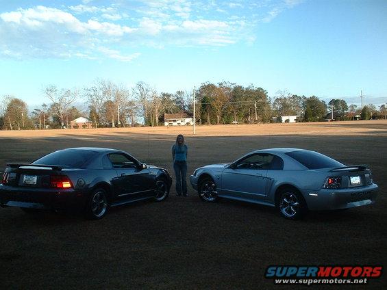 Two 1999 Ford Mustangs, one gray and one silver, parked in a field