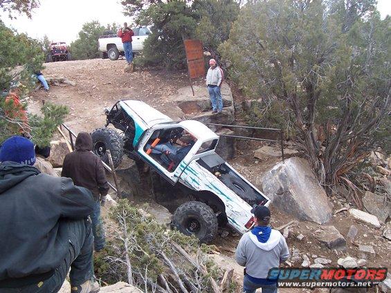 Custom rock crawler with big tires navigating a rocky trail. People are watching