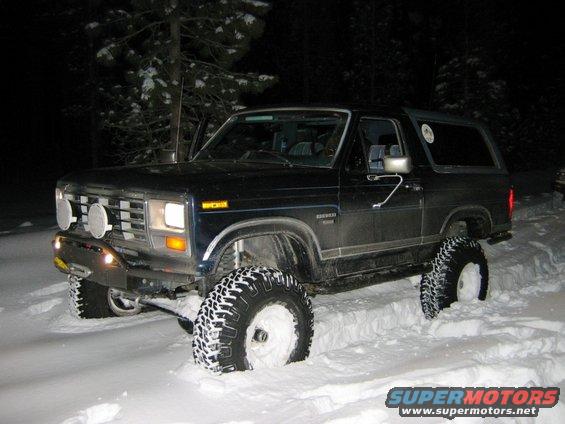 Dark blue Ford Bronco with lifted suspension and large tires in snow, front 3/4 view