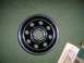 1985 Ford Bronco - A black wheel with chrome trim and ten circular cutouts is shown against a green background.