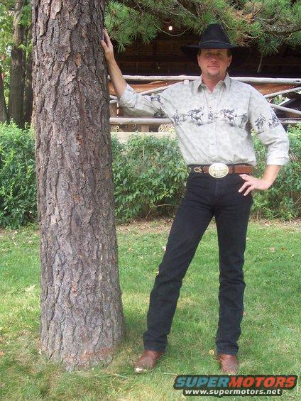 Man in cowboy hat leans against a tree