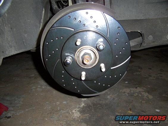 Brake rotor with drilled holes and slots, attached to a hub with lug nuts