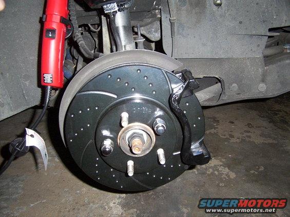 close-up of a car's front brake rotor and caliper, with a red heat gun nearby