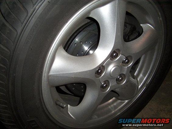 Close-up of a silver 5-spoke wheel with a perforated brake rotor visible behind it