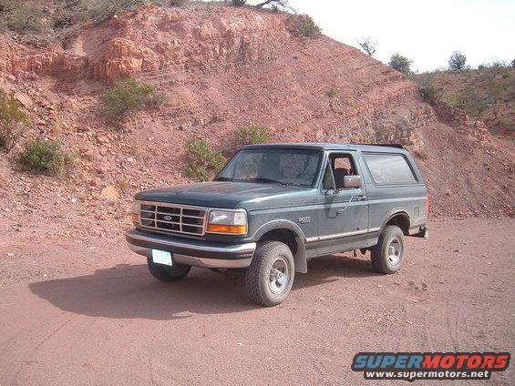 Green 1994 Ford Bronco parked on a dirt road with a red rocky hill in the background