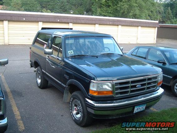 Dark blue Ford Bronco parked next to a green sedan in front of storage units