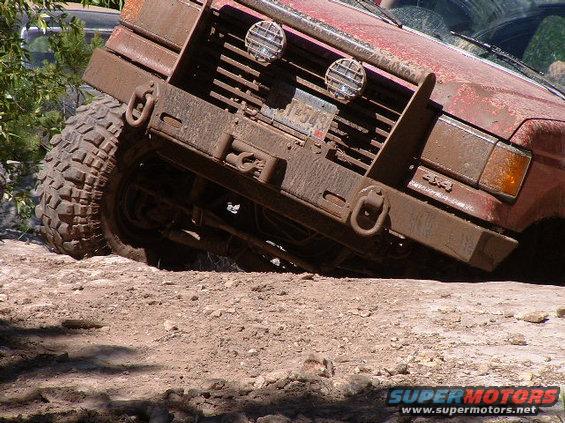 Mud-covered red off-road vehicle front view with large tires and winch