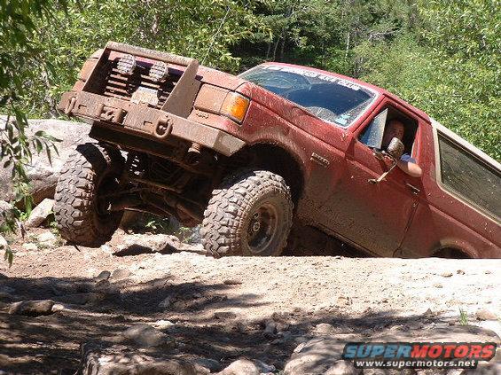 1989 Ford Bronco climbing over rocks on a dirt trail, driver visible