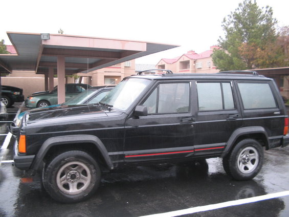Black Jeep Cherokee parked on wet asphalt under a carport