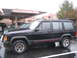1991 Ford Bronco - A black Jeep Cherokee is parked on a wet surface next to other vehicles.