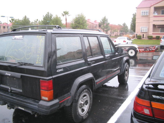 Black Jeep Cherokee 4x4 with red stripe detail, parked in a wet lot