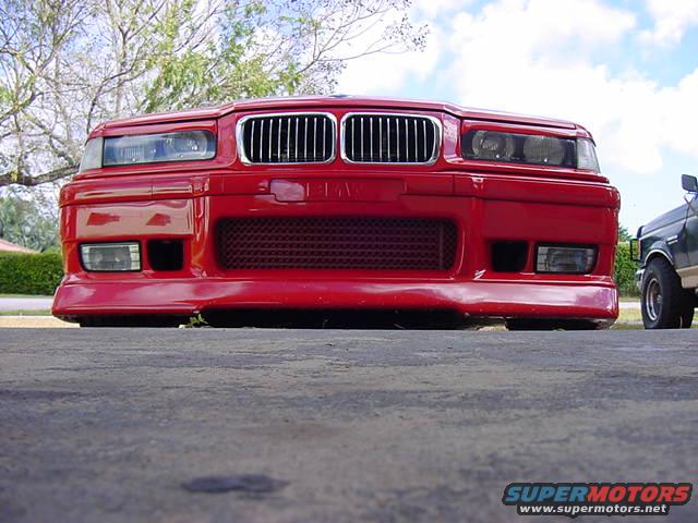 front view of red BMW sedan, parked next to a green pickup truck