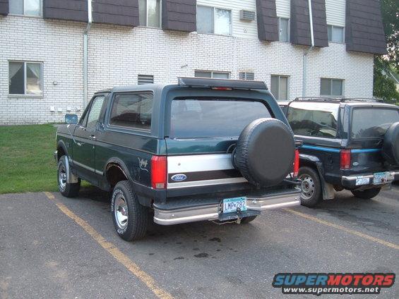 Green Ford Bronco parked next to another Bronco. Spare tire on the back of the green one
