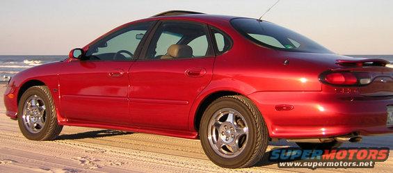1997 Ford Taurus sedan parked on a sandy beach with the ocean in the background