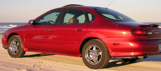 Red sedan parked on a sandy beach with the ocean in the background
