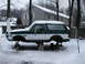 1994 Ford Bronco - A two-tone Ford Bronco sits on blocks and jack stands in the snow, missing its wheels.