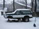 1994 Ford Bronco - A two-tone green and white 1994 Ford Bronco sits on jack stands in the snow, with its front wheels off.