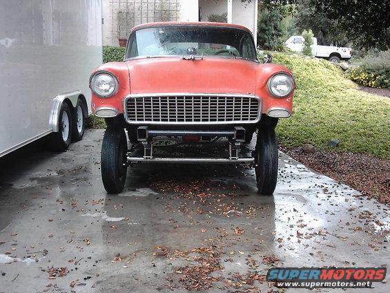Orange 1955 Chevrolet Bel Air with custom front end, parked next to a trailer. White pickup truck in background