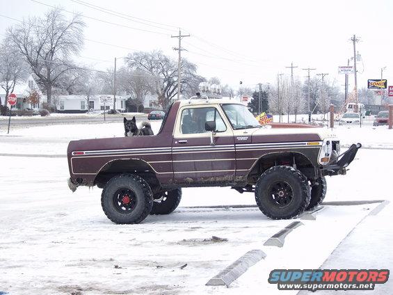 Maroon Ford pickup truck with a dog in the bed, parked in snow
