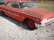 1963 Ford Galaxie - A vintage red Ford Galaxie coupe sits on a gravel lot, showing signs of age and wear.