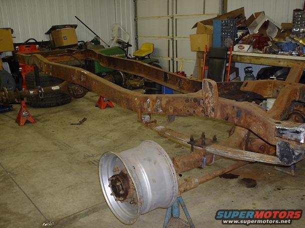 Rusted truck frame on jack stands in a garage, with a detached wheel in the foreground