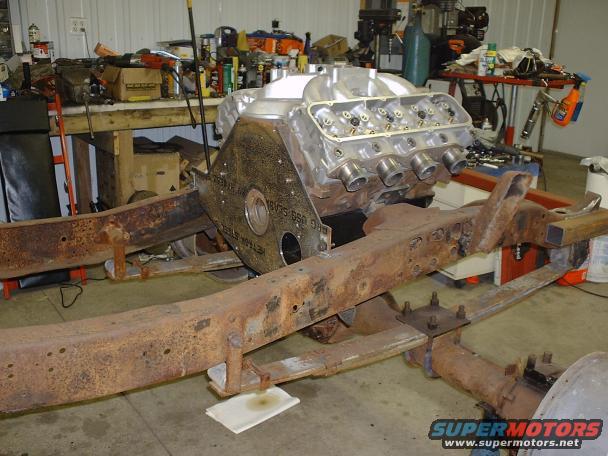 Engine block and rusty chassis in a workshop. Some tools and parts are on a workbench in the background