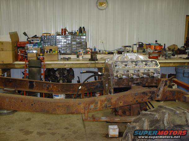 Rusty vehicle frame with a V8 engine assembly mounted on it in a workshop