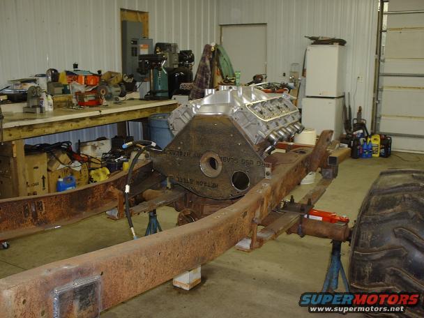 Engine block and rusty chassis frame on stands in a workshop. Text on engine block reads 'METRO STEEL'