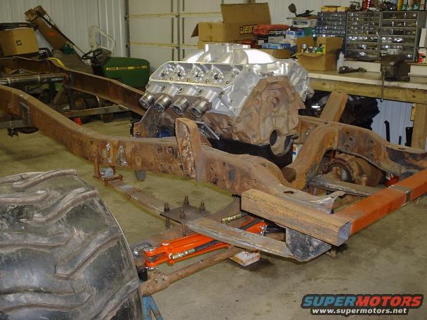 Truck frame in a garage with a large engine on top. A big tire is in the foreground