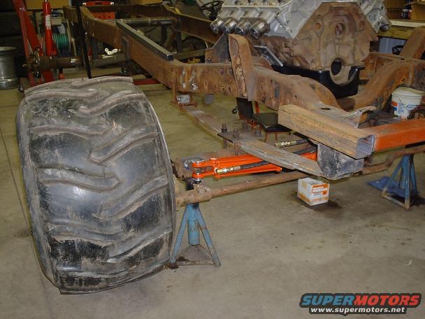 Truck chassis on jack stands with a large tire and V8 engine block visible