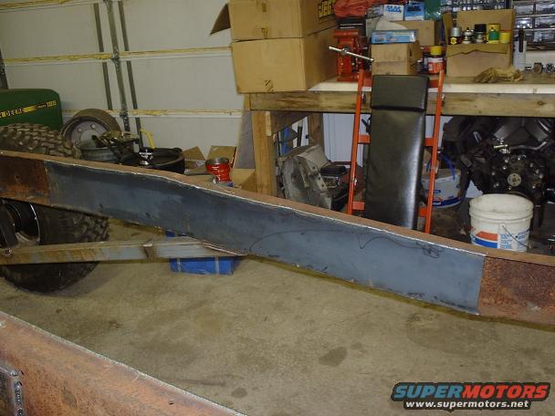 Truck frame section with a newly welded metal plate. Tires and a green tractor visible