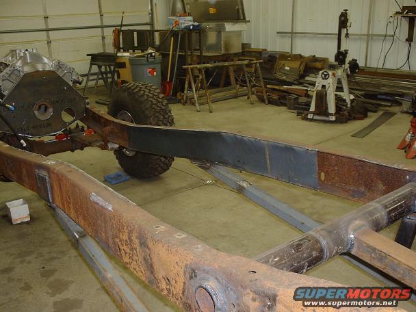Vehicle frame with engine and one tire visible, in a workshop setting. Some parts appear rusty