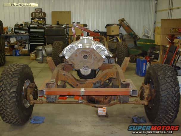 Vehicle frame with engine and large tires in a garage. Tools and other equipment are visible in the background