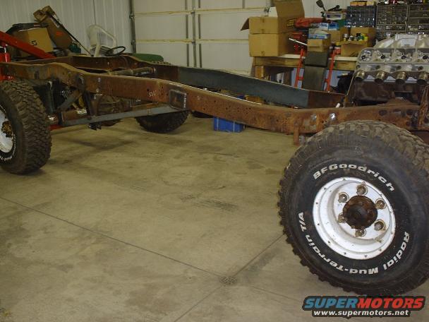 Truck chassis with rusty frame, BFGoodrich tires, and engine block. White rims are visible