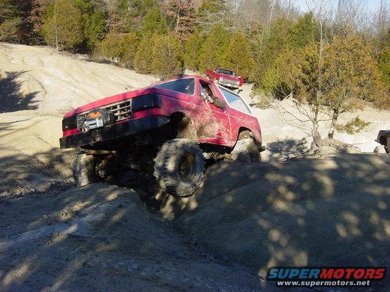 Red off-road SUV with large tires climbing a muddy hill