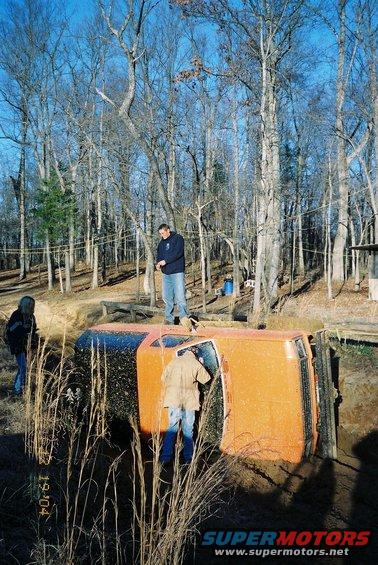 Orange SUV rolled onto its side in a muddy ditch with people around it. Date stamp reads 19.04