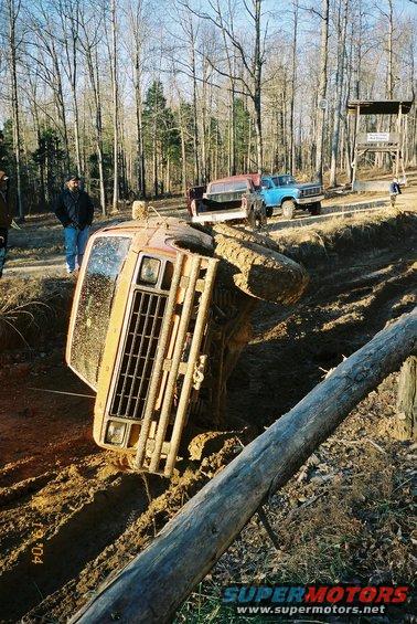 Orange off-road vehicle tilted on its side in mud, front grille and headlights visible