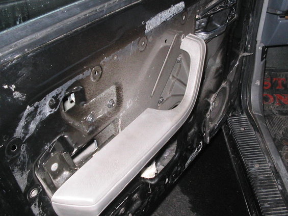 Black car door interior with removed panel, showing gray armrest and exposed metal