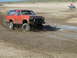 1993 Ford Bronco - Orange Ford Bronco navigates a muddy terrain, with an ATV visible in the distance.